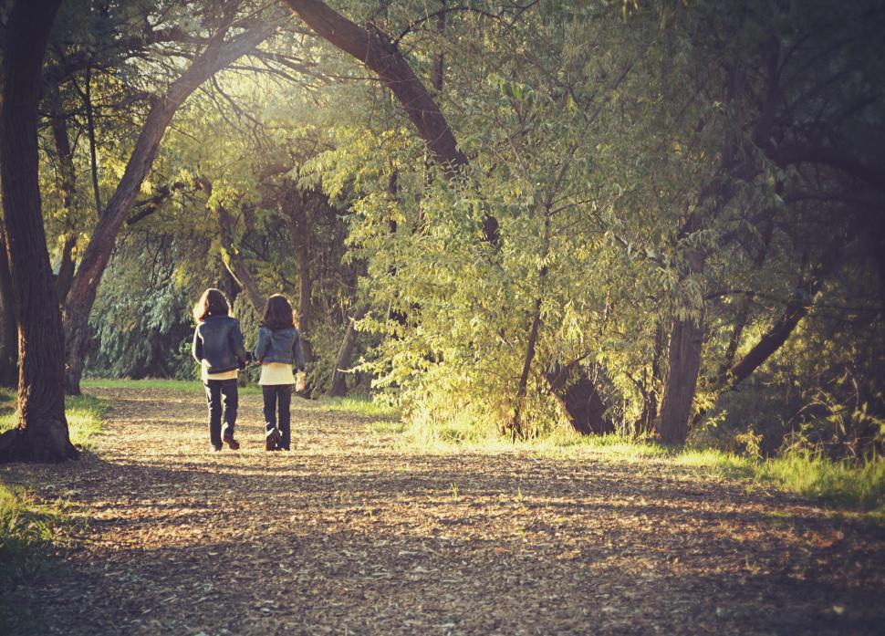Two friends walking side by side through a quiet park in the fall.